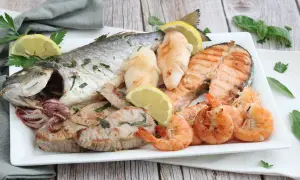 Un piatto invitante di grigliata di pesce: orata intera, tranci di salmone, gamberi, calamari e tonno, guarnito con limone e prezzemolo.