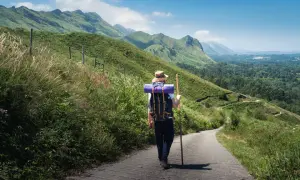 Pielgrzym w kapeluszu i z plecakiem idzie ścieżką przez zielone wzgórza. To jedna z malowniczych tras Camino de Santiago.