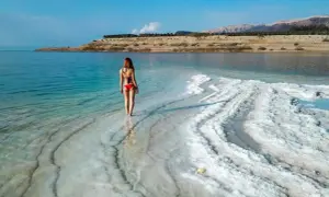 Kobieta w czerwonym bikini stoi na brzegu Morza Martwego, otoczona kryształami soli.