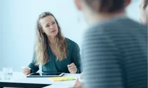 Frau mit Tablet und Stift im Gespräch mit unscharfen Personen.