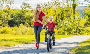 Mama uczy synka, jak nauczyć dziecko jeździć na rowerze. Radosny chłopiec pedałuje, a mama go asekuruje.