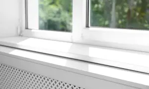 Biały parapet pod okno, z widocznym fragmentem grzejnika, odbija światło słoneczne.