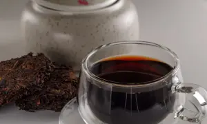 Ciemna, aromatyczna czerwona herbata w szklance, obok sprasowanych liści. Idealna do nauki, jak parzyć czerwoną herbatę.