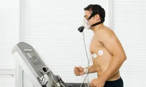 Mężczyzna w masce tlenowej i elektrodach EKG biegnie na bieżni podczas testu coopera.