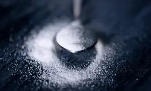 Łyżeczka z cukrem, symbolizująca ile cukru dziennie można spożyć, leży na ciemnym tle.