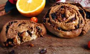 Due pitte nchiuse calabresi, dolci tradizionali con uvetta e noci, su un tagliere di legno con arancia e pomodorini.