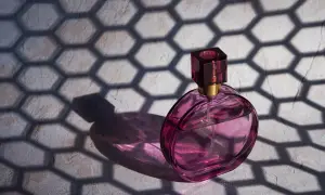 Różowa buteleczka perfum Dior J'adore, oświetlona słońcem, rzuca cień o geometrycznym wzorze plastra miodu.