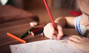 Bambina scrive con matita a pois rossi, circondata da pastelli. Forse sta calcolando l'indennità di frequenza scolastica importo.