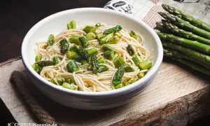 Spargel Pasta: Ein Teller Spaghetti mit frischen grünen Spargelstücken, daneben ein Bund Spargel.
