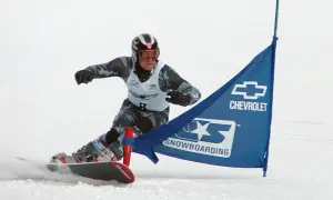 Snowboardzista w kasku i goglach mija niebieską flagę z logo Chevrolet. To sport, który zyskał popularność w XX wieku, choć jego korzenie sięgają wcześniejszych lat.