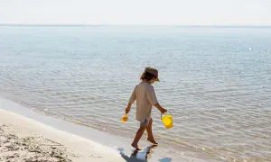 Barn med hink och spade vid havet, njuter av solen. Hoppas inte på solsting barn!