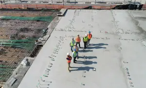 Grupa budowlańców na placu budowy, dyskutująca o tym, ile kosztuje kubik betonu. Widać zbrojenie i świeżo wylany beton.