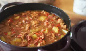 Un plat mijoté d'axoa de veau avec des pommes de terre et des poivrons rouges, servi dans une cocotte.