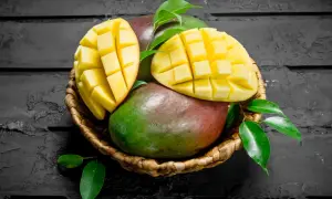 Koszyk z dojrzałymi mango, jedno przekrojone na pół, ukazujące soczysty miąższ. Interesuje Cię mango indeks glikemiczny?