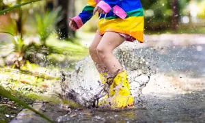 Bambino con stivali gialli salta in una pozzanghera, creando spruzzi d'acqua. Ecco perché i bambini si sdraiano per terra: per godersi il gioco!