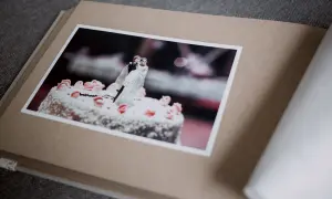 Otwarty album z fotografią tortu weselnego i figurkami pary młodej. Różne rodzaje papieru tworzą jego okładkę i strony.