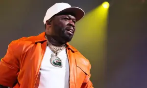 50 Cent w pomarańczowej kurtce i białej czapce, z błyszczącym naszyjnikiem, występuje na scenie. Polska publiczność szaleje!