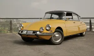 Citroën Tiburón amarillo, un clásico icónico con su diseño aerodinámico y faros distintivos, aparcado en un mirador con vistas a la ciudad.
