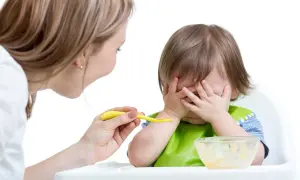 Mama próbuje nakarmić dziecko, ale maluch zakrywa buzię rączkami. Wygląda na to, że 8-letnie dziecko nie chce jeść.