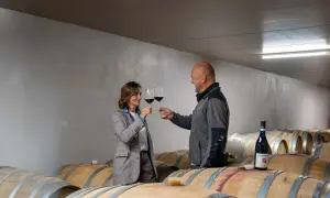 Un uomo e una donna brindano con calici di vino rosso tra le botti nella provincia del Barolo.