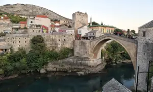 Stari Most, en ikonisk stenbro i Mostar, sträcker sig över en turkos flod. Gamla stenbyggnader och en moské omger den.