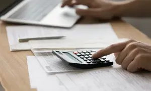 Mano che usa una calcolatrice per capire come si calcola la RAL, con laptop e fogli sparsi.