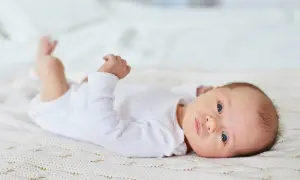 En bebis med blå ögon ligger på en stickad filt. Bebis andas snabbt, dess små händer knyts.