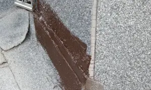 Brązowy lepik uszczelnia dach. Widać metalowy element odpływu.