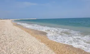 Spiaggia di ciottoli a Civitanova Marche, con il mare azzurro e le onde che lambiscono la riva.