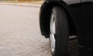 Błyszczące, czarne auto na kostce brukowej. Widoczna opona zimowa, której wiek można ocenić po bieżniku.