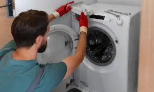 Serwisant w czerwonych rękawiczkach wyjmuje szufladę dozownika z pralki LG, która wyświetla błąd OE.