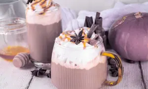 Dwie pyszne pumpkin spice latte kawa z bitą śmietaną, karmelem i cynamonem. Obok dynia i miód.