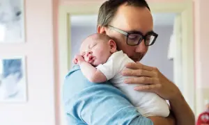 Ojciec delikatnie tuli śpiącego noworodka na ramieniu. To idealny moment, kiedy odbijać noworodka, by zapewnić mu spokój i komfort.