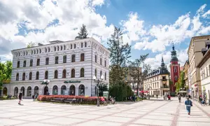 Słoneczny dzień na placu w parku zdrojowym w Cieplicach Śląskich-Zdroju. Ludzie odpoczywają na ławkach, spacerują.