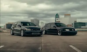 Dwa czarne Volkswageny: sportowy hatchback GTI i obniżony sedan, stoją na parkingu z widokiem na miasto.