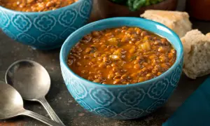 Bol de soupe de lentilles savoureuse, une recette réconfortante avec du pain et des couverts.