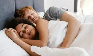 A couple sleeps peacefully, their bodies intertwined. Do you sleep better next to someone you love?