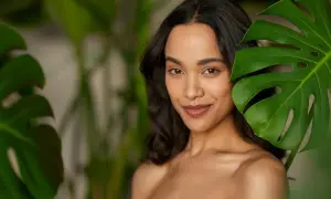 Mujer con maquillaje efecto bronceado, sonriendo entre hojas verdes.