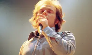 Van Morrison sings passionately into a microphone, his eyes closed. This image captures a moment from one of his legendary performances, perhaps hinting at the setlists that have defined his career.