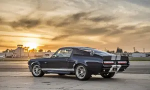 Elegancki, ciemny mustang Eleanor z białymi pasami na masce i dachu, zaparkowany na lotnisku o zachodzie słońca.