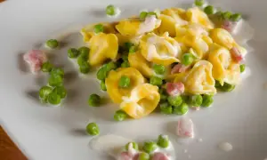 Tortellini di carne con piselli e pancetta, un classico condimento per un primo piatto gustoso e cremoso.