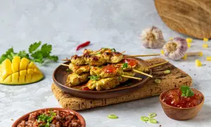 Aksamitne satay z kurczaka na patyczkach, polane sosem, obok ryż, mango i czosnek.