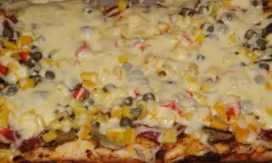 Pyszna pizza na grubym cieście z warzywami i roztopionym serem.
