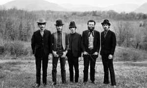 The Band, who wrote "The Weight," pose in a field with mountains in the background.