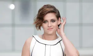 Kristen Stewart w białej sukience z czarnym wykończeniem, poprawia włosy. Aktorka znana z wielu filmów.
