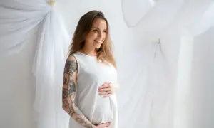 Uśmiechnięta ciężarna kobieta z tatuażem na ramieniu. Czy można zrobić tatuaż w ciąży? To pytanie nurtuje wiele przyszłych mam.