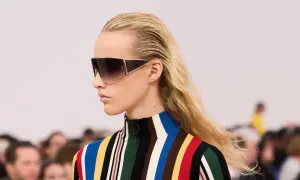 Modelka w okularach i bluzce w kolorowe pasy, zapowiadająca odważną modę 2026.
