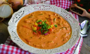 Aksamitna zupa gyros z kurczakiem i pieczarkami, udekorowana kolorową papryką i natką pietruszki. Obok leżą cebule i czosnek.