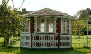 Pavillon de jardin rouge et blanc, orné de dentelle de bois. Une pomme tombe d'un arbre, peut-être pour échapper à la taxe abri de jardin.