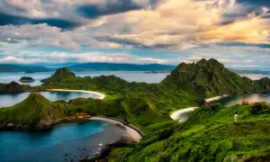 Grüne Hügel und weiße Sandstrände im Komodo Nationalpark, Indonesien. Ein einsamer Wanderer genießt die atemberaubende Aussicht auf das Meer.